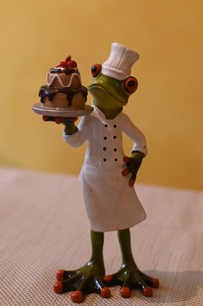 Frosch als Konditor gekleidet, der einen Kuchen hoch hält.